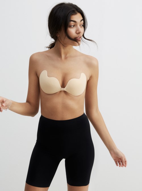 A woman wears a beige strapless top and black high-waisted shorts, standing sideways with a neutral background.
