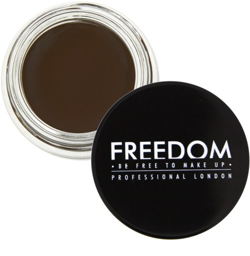 En svart rund beholder med orden "FREEDOM" og "BE FREE TO MAKE UP" på lokket, ved siden av en åpen krukke med brunt sminke.