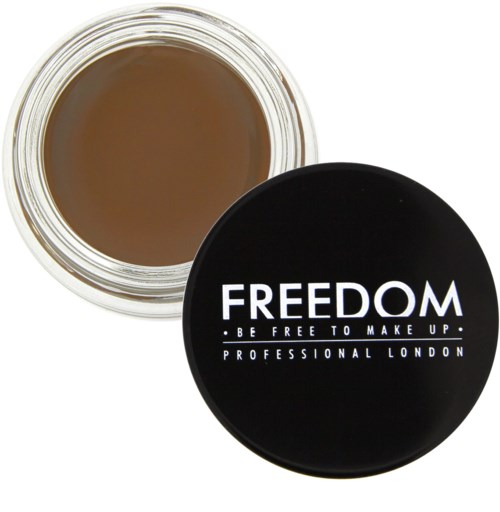 En liten rund beholder med brunt makeup-innhold og svart lokk med hvit tekst som sier "FREEDOM," "BE FREE TO MAKE UP," og "PROFESSIONAL LONDON."