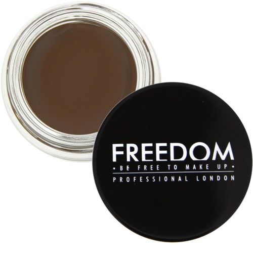 Et svart lokk med hvit tekst som sier "FREEDOM" og "BE FREE TO MAKE UP" med et glass med brunt sminke inni.