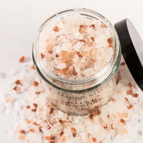Pink Himalayan salt in a glass jar with a black lid, surrounded by scattered salt crystals.
