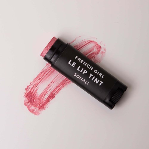 A black lip tint stick with white text, lying on a pink smear of color on a white background.