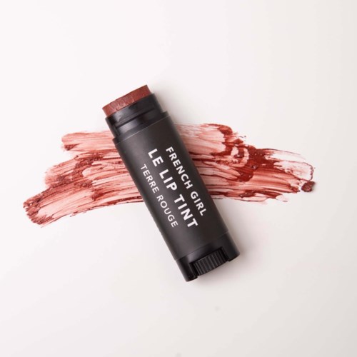 Lip balm tube labeled 'French Girl Lip Tint' with reddish color. Cream spread on white background.