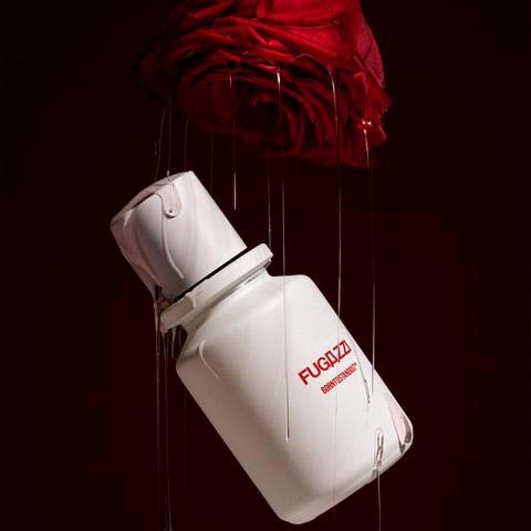 A white bottle with red text hangs nearby a red cloth blanket against a dark background.