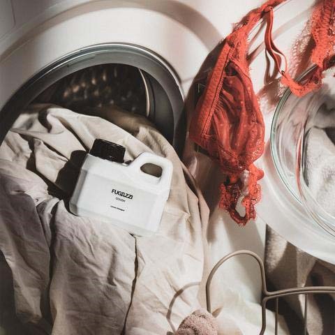 Clothes inside a washing machine, with a container and red fabric nearby, indicating laundry or washing process.