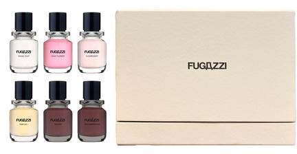 Sześć małych butelek perfum z czarnymi nakrętkami, oznaczonych FUGAZZI, znajduje się w beżowym pudełku. Trzy butelki są różowe, żółte i fioletowe.