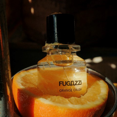A perfume bottle labeled 'FUGDZZI ORANGE CRUSH' sits inside half an orange fruit.