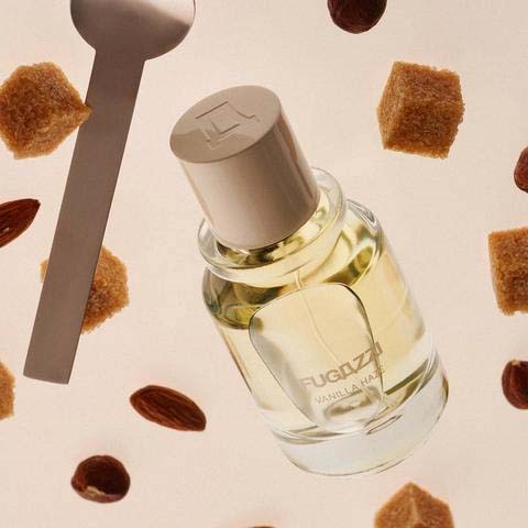 A bottle of vanilla perfume surrounded by sugar cubes and almonds, with a spoon nearby.