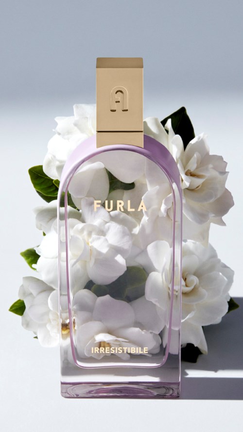 En parfyllflaska märkt 'FURLA' och 'IRRESISTIBILE' omgiven av vita blommor och gröna blad.