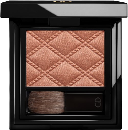 En sminkkompakt med quiltad blush i persikfärg och en borste under den i ett svart kvadratiskt fall.