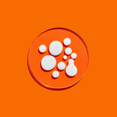 White pill shapes of different sizes on an orange background, inside a clear round dish.
