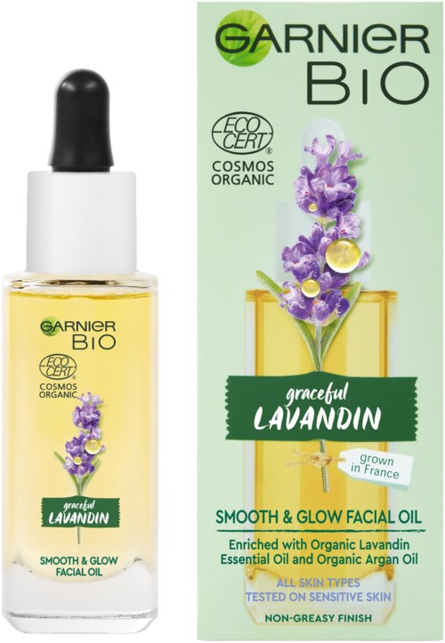 A facial oil product with a dropper, bottle, and green packaging featuring lavender flowers and text about organic ingredients.