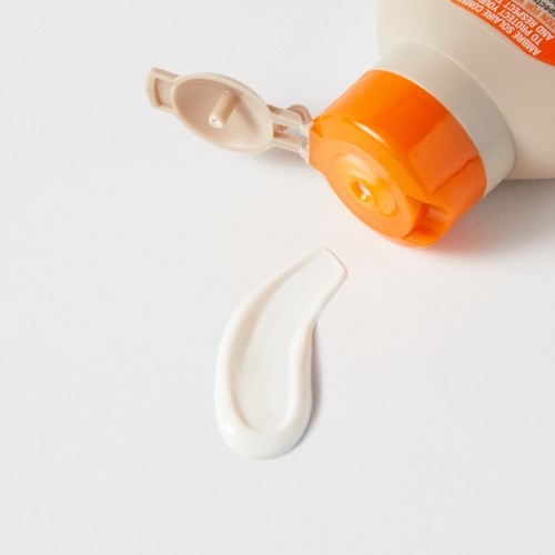 A white and orange lotion or cream bottle with its cap open, and a dollop of cream on the surface.