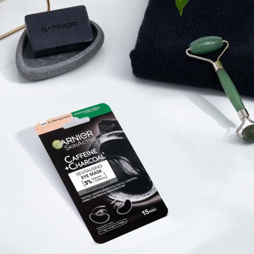 A black soap, a green jade roller, a face towel, and a charcoal eye mask package on a white surface.