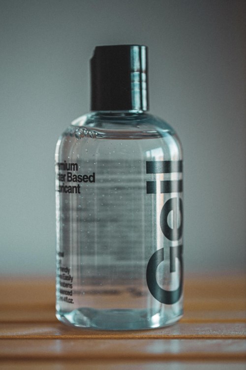 A transparent bottle filled with clear liquid, labeled with black text, standing on a wooden surface.