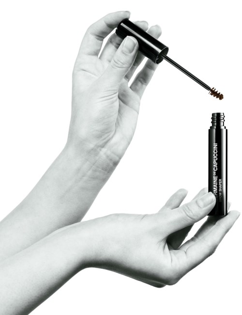 Een persoon houdt een mascara-flacon en borstel, klaar om make-up op de wimpers aan te brengen.