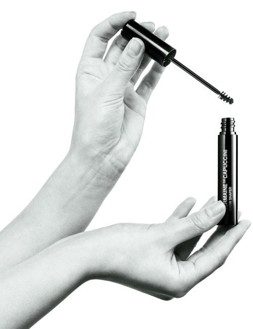 Twee handen houden een mascara-flacon en kwast, klaar om make-up aan te brengen.