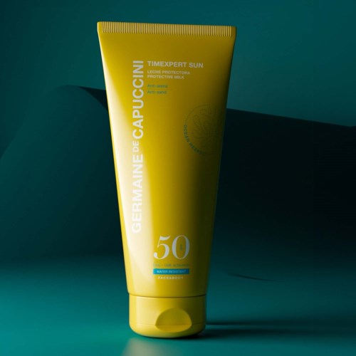 En gul solkremtube med SPF 50, merket 'Germaine de Capuccini' og 'TIMEXPERT SUN,' står på en grønn overflate.