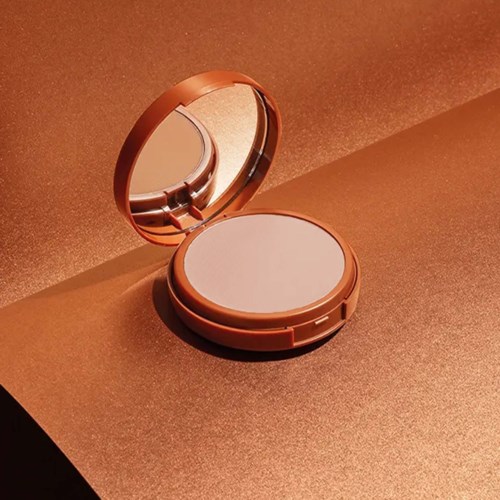 En kompakt sminkespeil med rose gull finish, åpen for å vise speilet inni på en brun overflate.