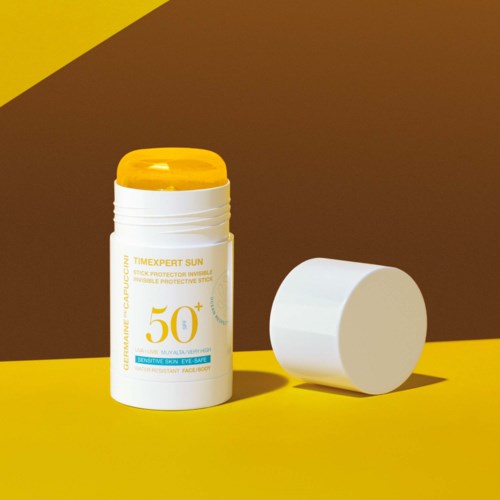 Pojemnik na krem do opalania z żółtą pokrywką, oznaczony SPF 50+, na tle żółto-brązowym.