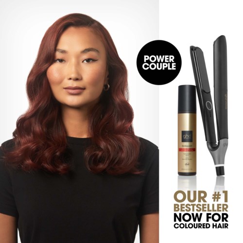 En kvinna med stylat röd hår, svart tröja och mjuk makeup, bredvid hårstylingverktyg och hårspray.