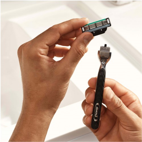 A person holds an electric razor and a shaving brush over a white sink.
