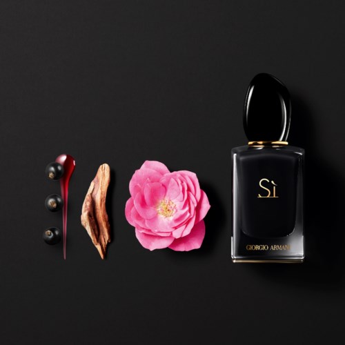 En svart parfymflaska märkt 'Sì' av Giorgio Armani, omgiven av mörkröda och svarta dekorativa element och en rosa blomma.