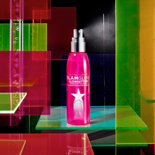 Rosa Glowsetter sprayflaska på färgglad, geometrisk bakgrund med ljusa, neonlika ljus.