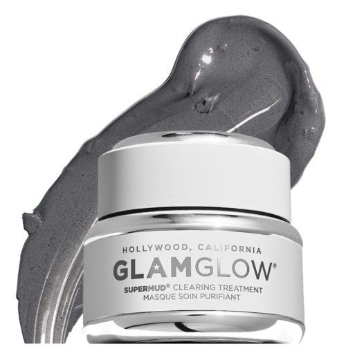 En vit burk märkt 'GlamGlow' med svart text, innehållande en skönhetsprodukt, placerad på en grå smeta-bakgrund.