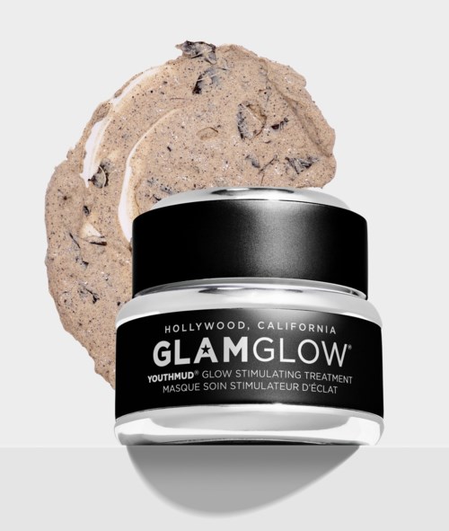 En glasburk med GlamGlow YouthMud ansiktsmask med en beige, sprucken mask bakom. Enkel, ren bakgrund.