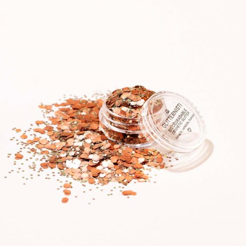 Small container of glitter with orange and silver shiny pieces spilled around it.