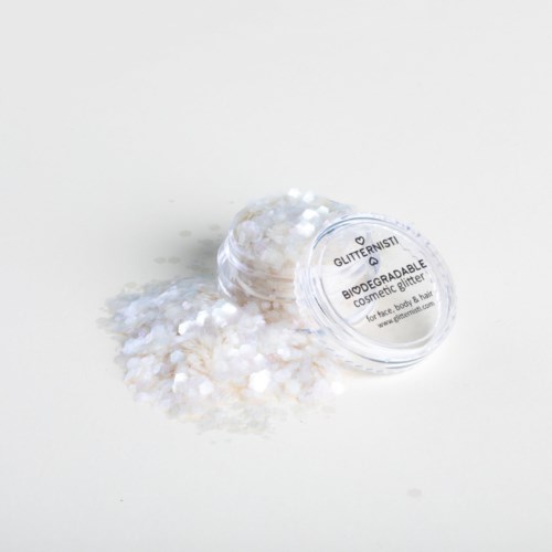 Ett litet genomskinligt förvaringsglas med glitter, som spillts ut på en vit yta.