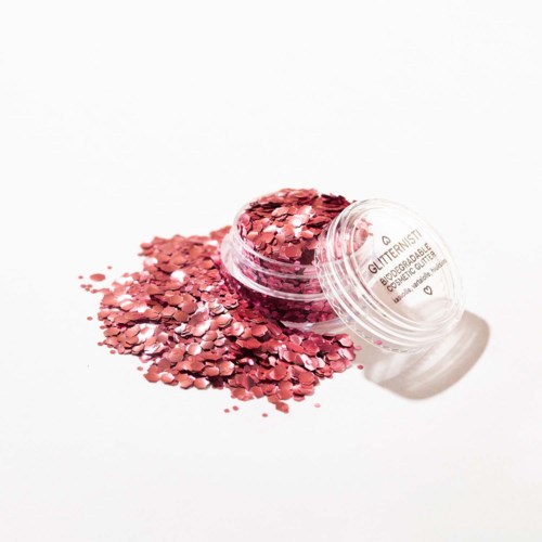 Ett runt öppet behållare med rosa glitter som spills ut på en vit bakgrund.