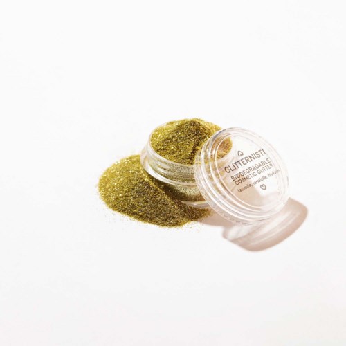 Small transparent container with shiny green glitter spilled outside. Labels indicate cosmetic or makeup use. Bright, simple background.