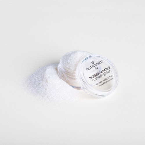 Ett genomskinligt behållare märkt 'Glittermusi' ligger på vit yta, spilld vit glitter omkring.