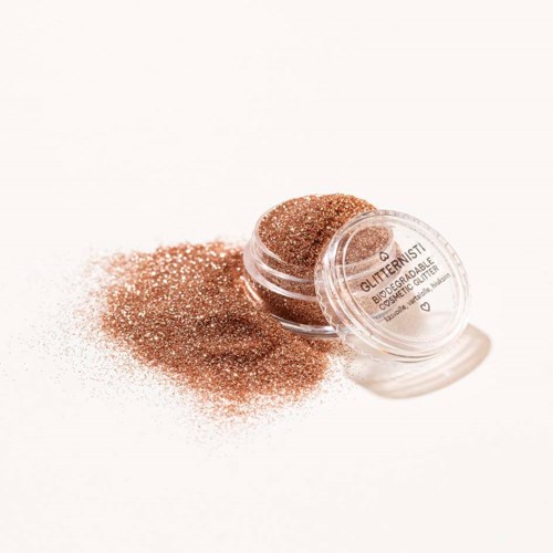 A container of glittery bronzer with some spilled powder on a white surface.