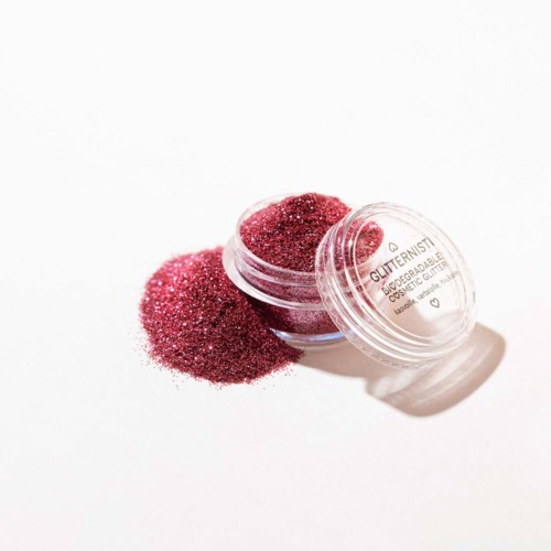 Pieni pyöreä rasia, jossa on pinkkiä glitteriä, ja osa on liukunut ulos valkoiselle taustalle.