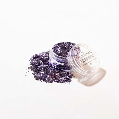 Ett litet öppet behållare med lila glitter som spillts ut på en vit yta.
