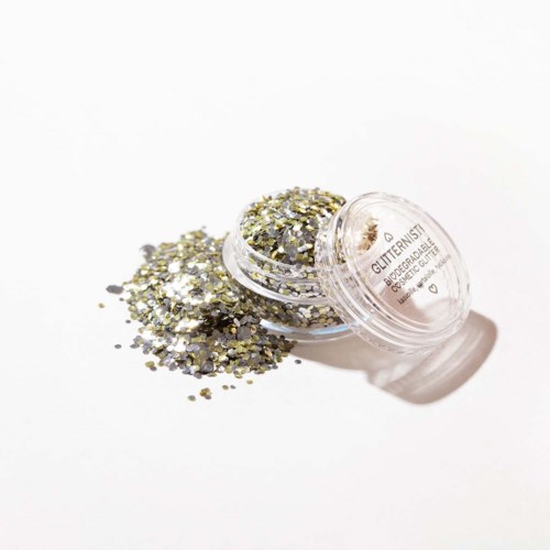 Small container with silver and gold glitter spilled on white surface.