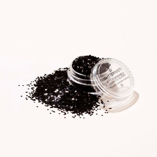 En liten rund behållare fylld med svart glitter, lite spilld utanför på en vit yta.