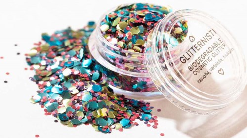 Färgglatt glitter i ett litet genomskinligt lock, några spillda på en vit yta.