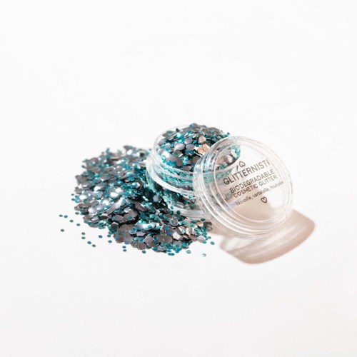 En liten behållare med blå och svarta glitter som är spillt på en vit yta.