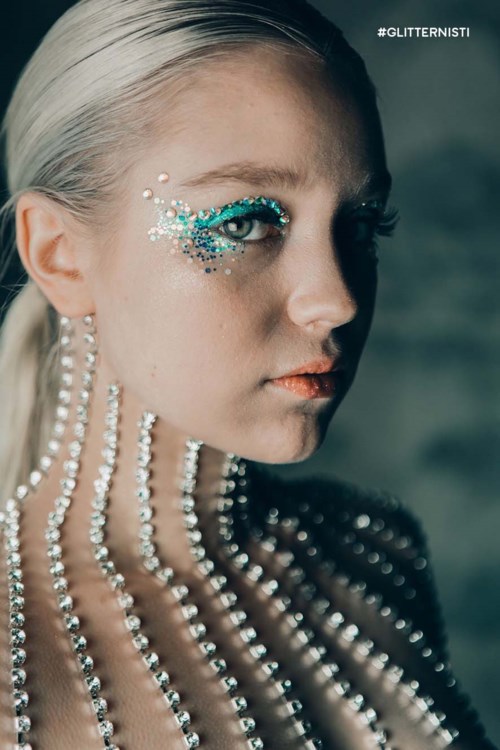 A woman with shiny makeup and pearl decorations on her face and neck, looking sideways.