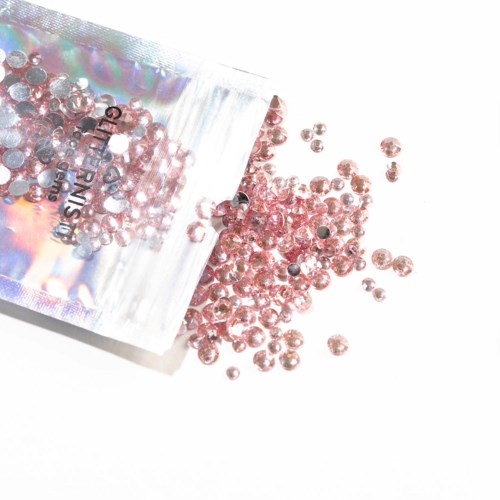 Pink rhinestones spilling from a clear plastic bag, scattered on a white surface.