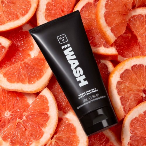 A black tube labeled 'WASH' surrounded by sliced grapefruits, suggesting a citrus-themed product or skincare item.