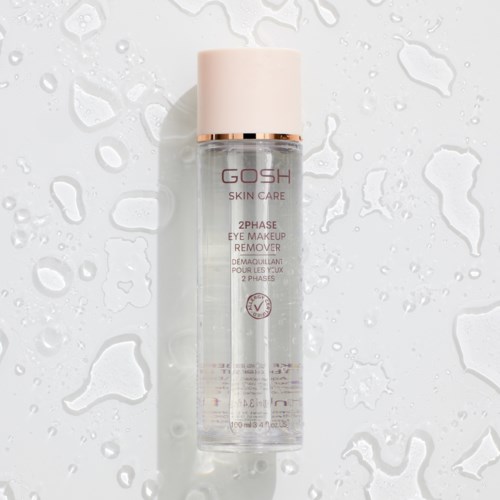 Läpinäkyvä pullo vaaleanpunaisella kannella, merkinnällä GOSH SKIN CARE 2PHASE EYE MAKEUP REMOVER, märkäpinnan päällä.