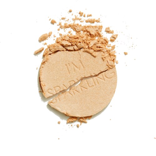 Rikki mennyt ympyrän muotoinen beige puuterirasia ja irtonaisia puuterihiutaleita valkoisella taustalla.