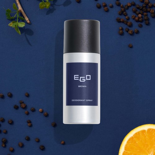 Deodoranttipullo, jossa tummanvärinen korkki, ympärillä mustapippureita, appelsiiniviipale ja vihreitä lehtiä.