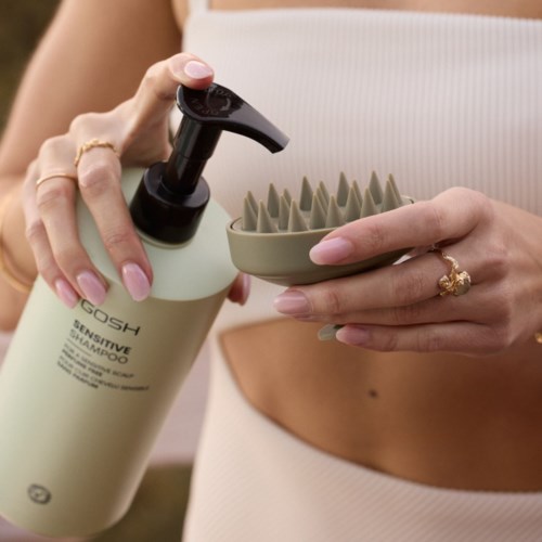 Henkilö pitää herkkä shampoo-ainetta ja silikonista päänahkan kuorinta-ainetta.