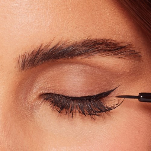 En person påfører sort eyeliner på øvre øjenlåg med en fin pensel.
